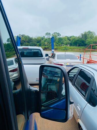 Auf einer Fähre (Argentinien nach Paraguay) aus dem Beifahrerfenster eines Vans heraus nach vorne auf die anderen Autos und das andere grün bewachsene Ufer schauend.