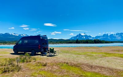 Ein Reisender steht auf einem Fels in einem türkisblauen See und schaut in die Ferne. Umliegend ein atemberaubendes Bergpanorama. Aufgenommen ist das Foto im Parque Nacional Tierra del Fuego.