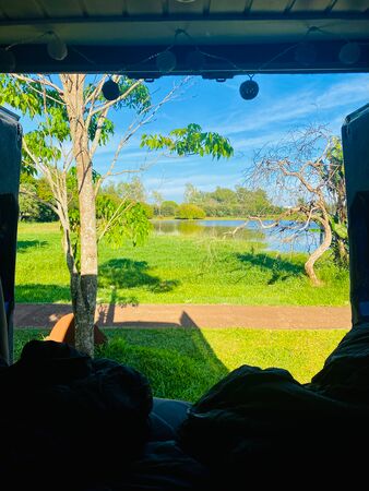 Ein idyllischer Blick aus dem Camper auf eine grüne Landschaft mit Bäumen, einer Wiese und einem Fluss bei Ciudad del Este in Paraguay, aufgenommen bei strahlend blauem Himmel und Sonnenschein.