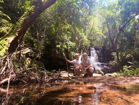 Zwei Personen posieren glücklich vor einem kleinen Wasserfall im Ybycuí-Nationalpark in Paraguay, umgeben von dichtem, grünem Dschungel und einem klaren Bach.